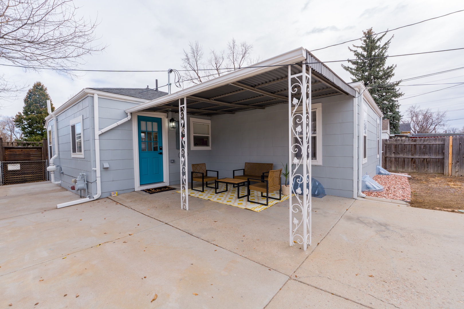 Modern rental property featuring covered outdoor seating area with stylish patio furniture and bright teal entrance door.