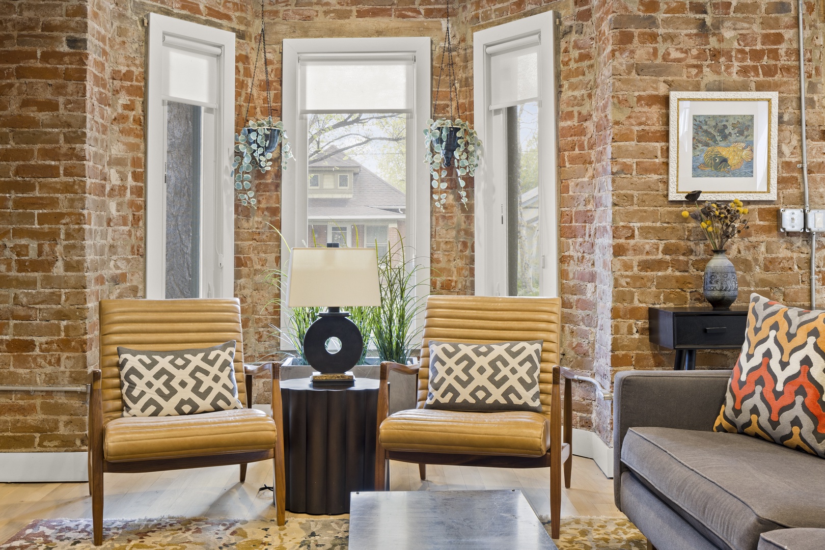 Relax in your stylish living room featuring exposed brick walls, vintage leather chairs, and curated artwork that creates the perfect urban retreat.