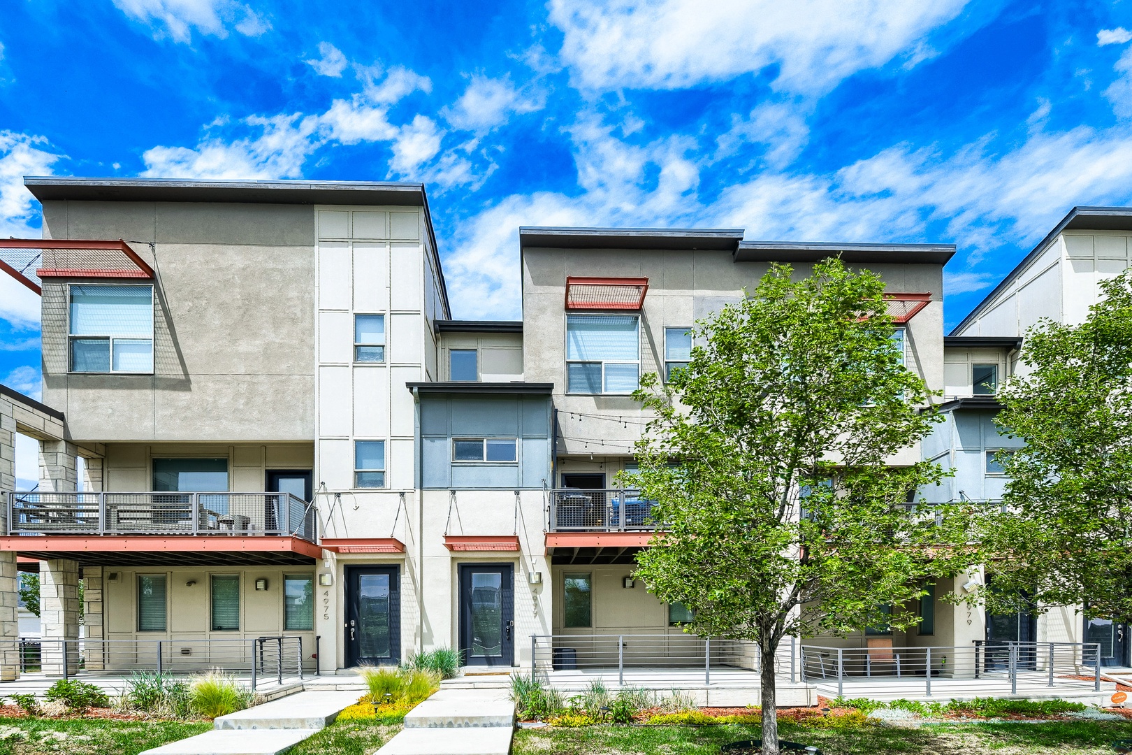 Modern multi-story townhomes feature contemporary architecture with clean lines, natural landscaping, and welcoming private entrances in a residential neighborhood setting.