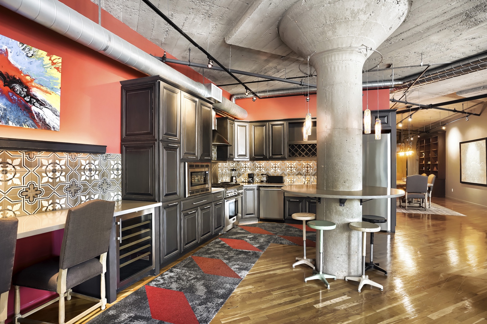 Step into your open loft-style kitchen featuring sleek dark cabinetry, stainless steel appliances, and vibrant coral accents that bring warmth to this modern industrial space.