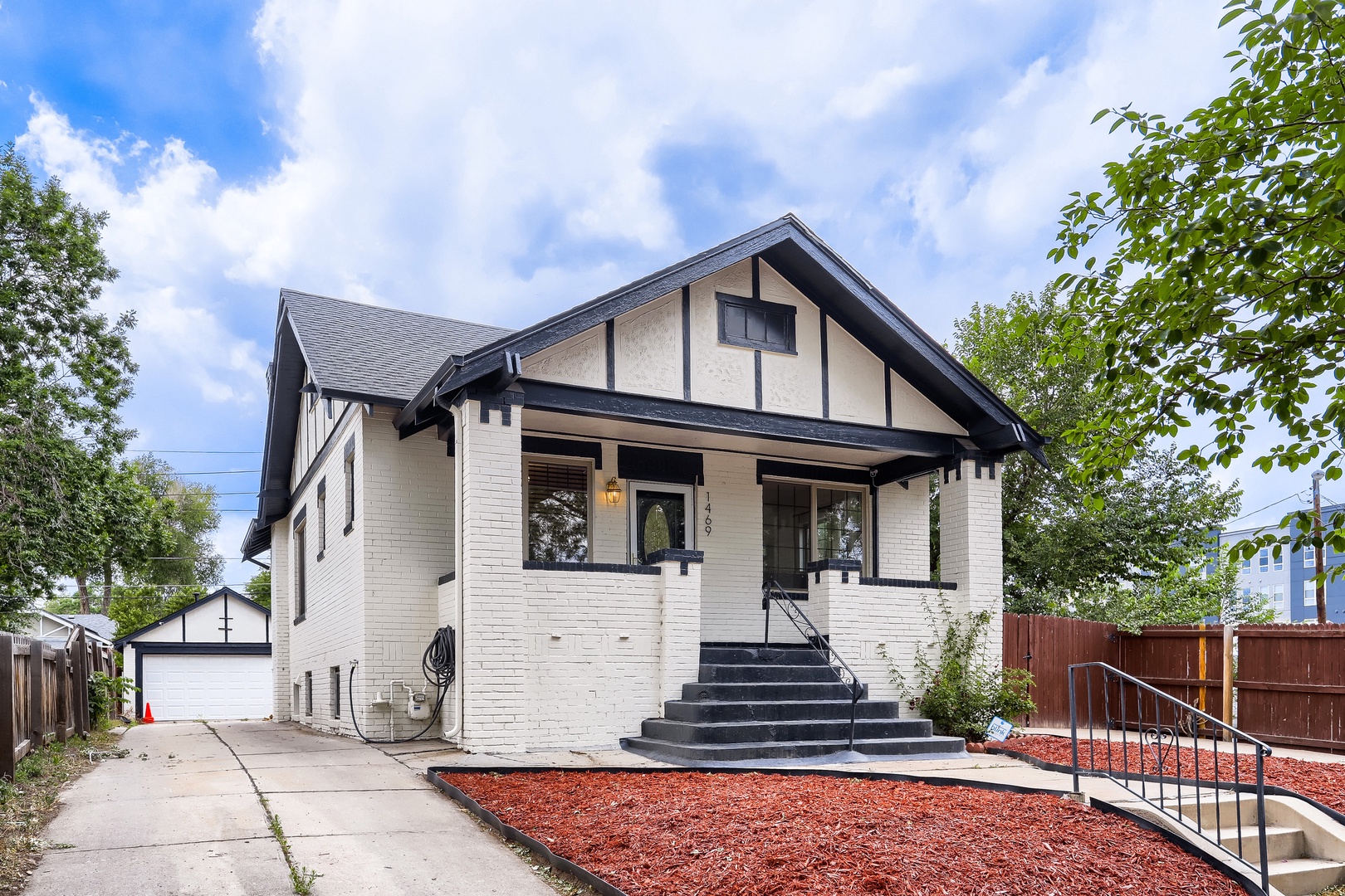 A charming craftsman-style home with fresh white exterior and classic dark trim, featuring a welcoming covered front porch and mature trees framing the property.