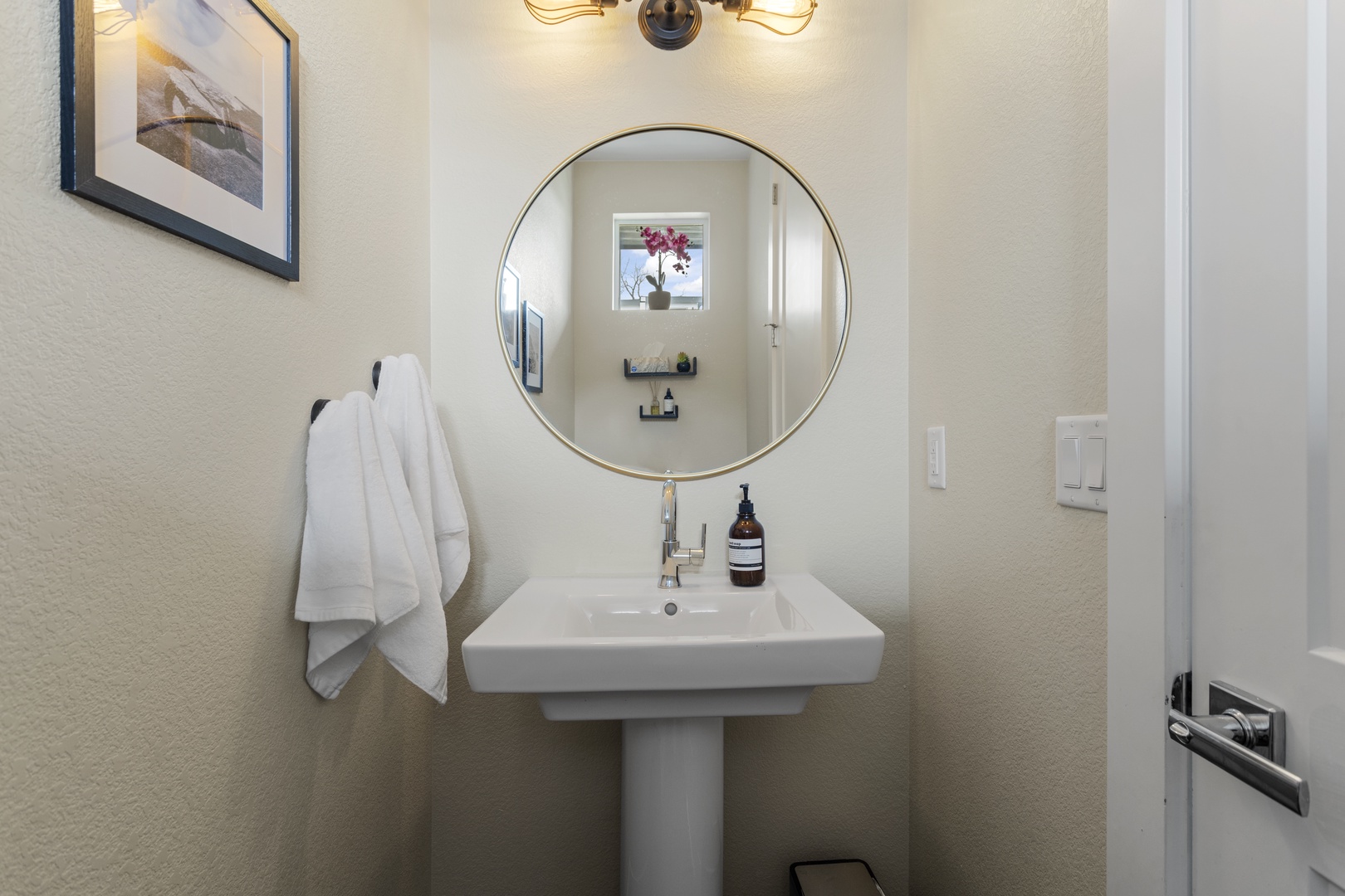 Step into your stylish powder room featuring a sleek pedestal sink, round gold mirror, and warm lighting for your comfort.