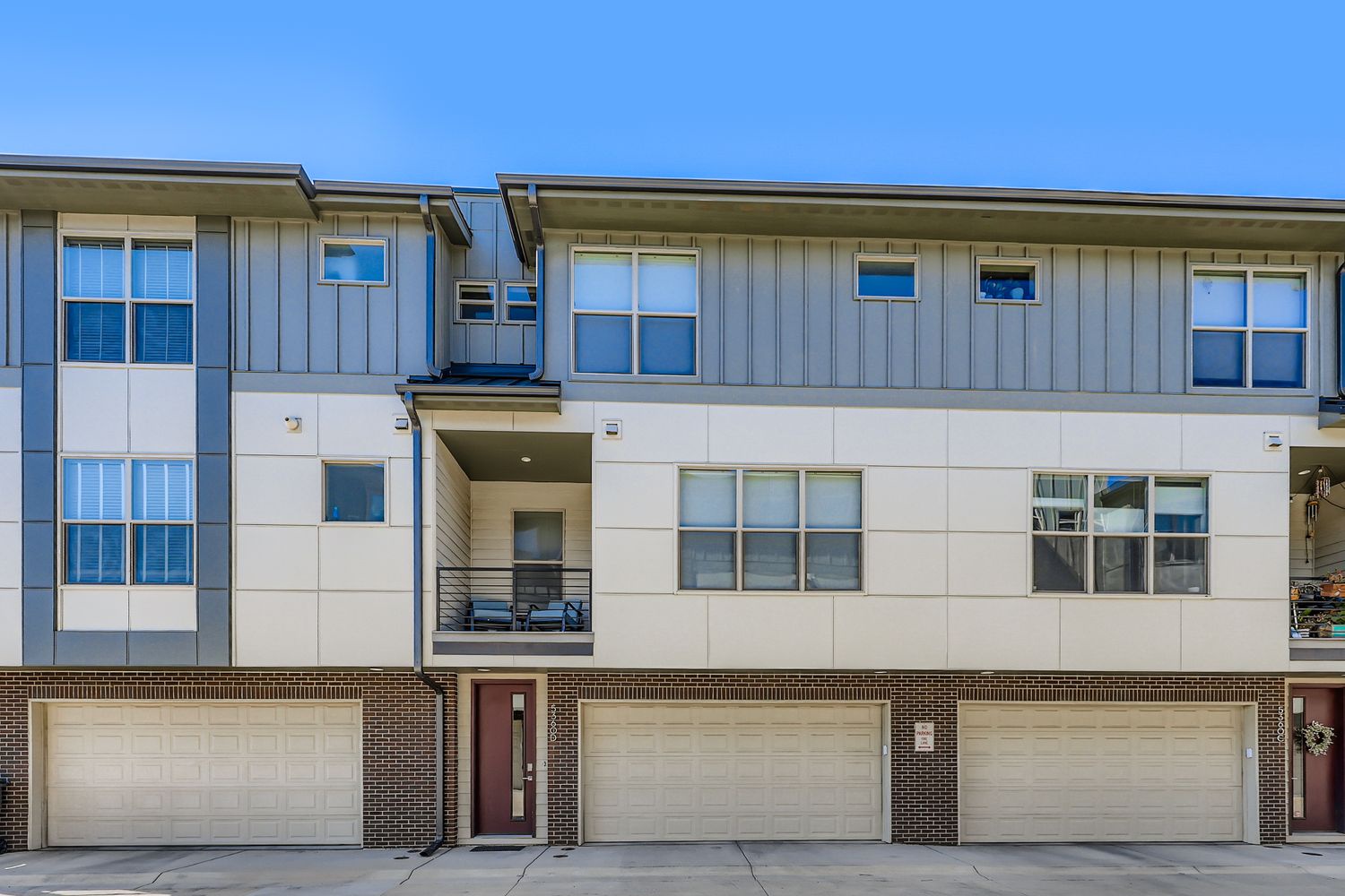 Modern townhome-style building with garage access under clear blue skies. The property features contemporary architecture with multiple units and spacious balconies.