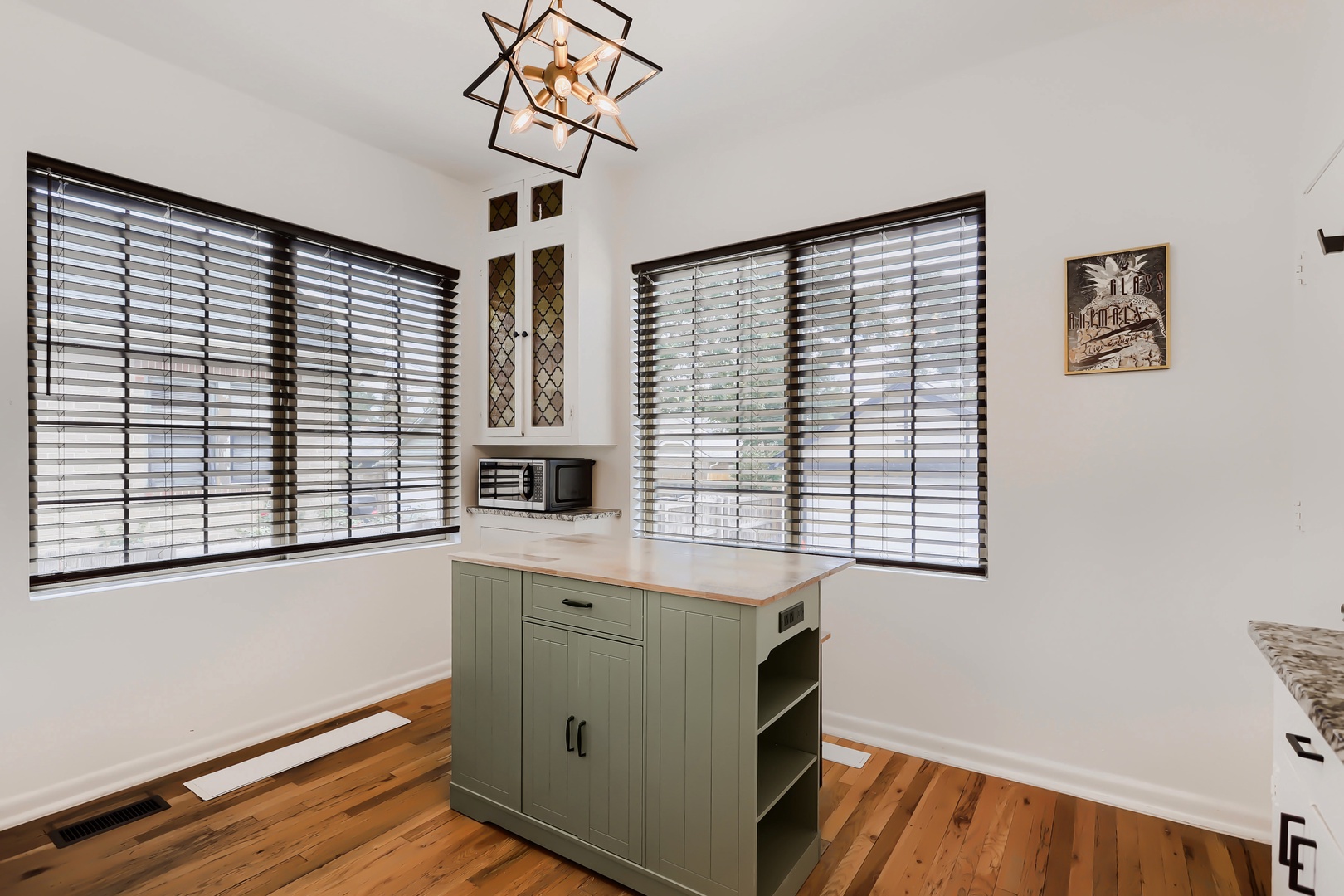 Your bright kitchen welcomes you with natural light streaming through large windows, gleaming hardwood floors, and charming details like the geometric pendant fixture overhead.
