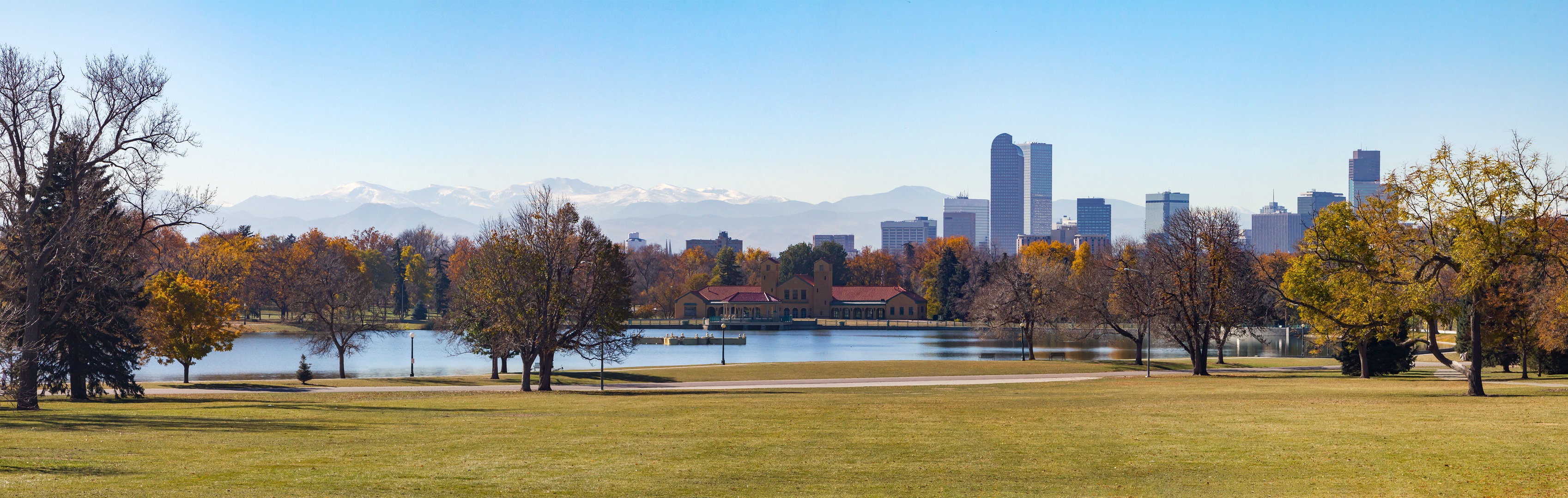 Denver's skyline rises beyond City Park's lake, with autumn colors and snow-capped Rockies completing this scenic urban landscape.