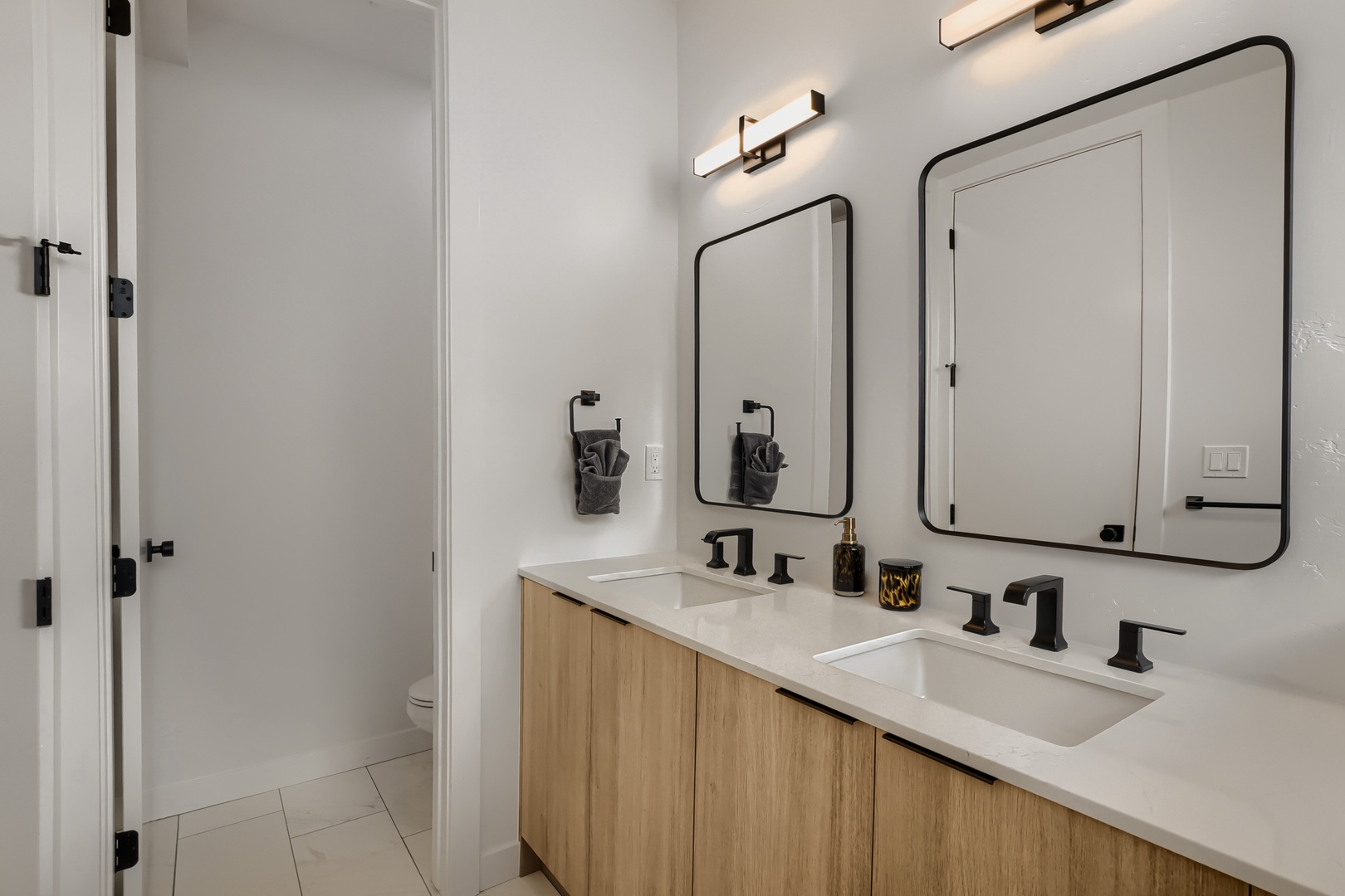 Your modern bathroom features dual vanities with warm wood cabinetry, elegant black fixtures, and a spacious walk-in shower—perfect for refreshing after a day of adventure.