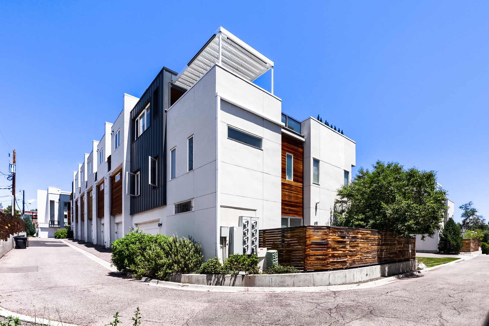 Modern townhome complex featuring contemporary architecture with wood accents and rooftop terrace, situated in a quiet residential neighborhood.