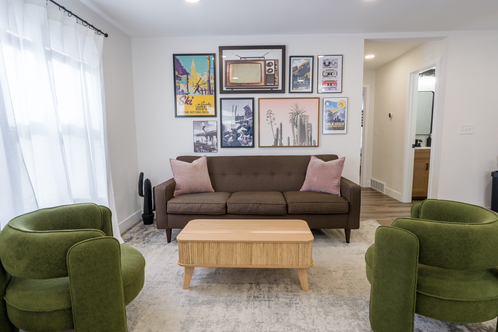 Settle into your stylish living space with plush green armchairs and curated gallery wall—perfect for cozy evenings or morning coffee.