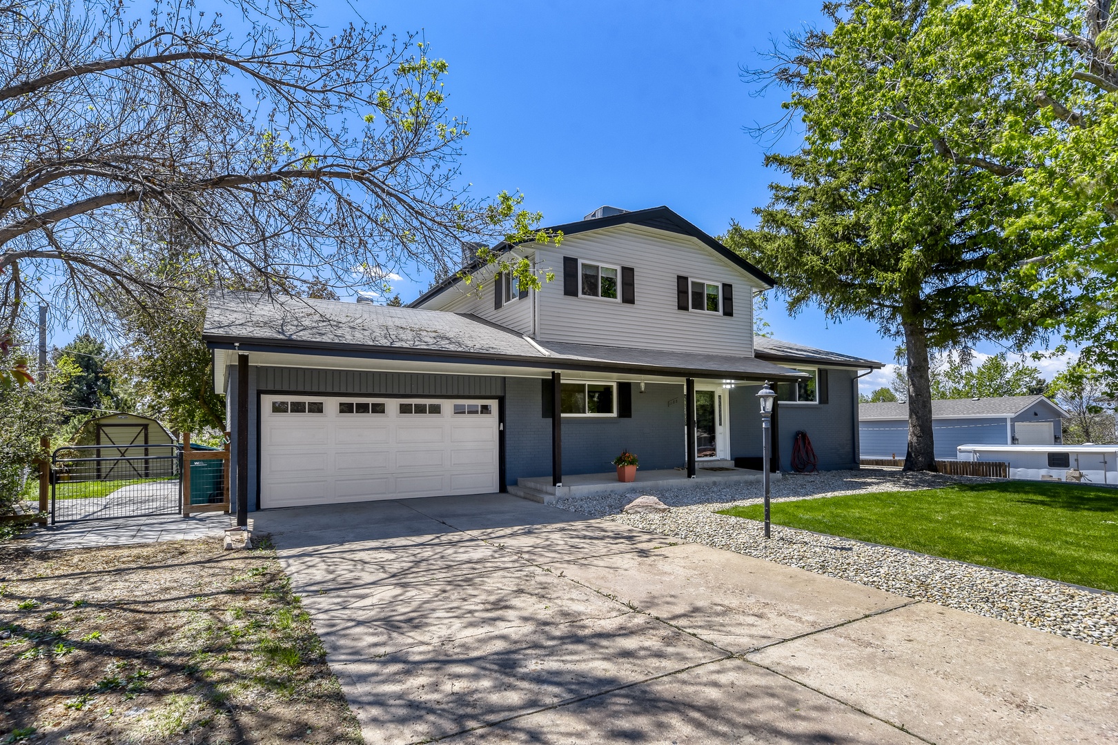 This two-story home features a modern gray and white exterior with black shutters, a spacious two-car garage, and mature trees framing the property in a quiet residential setting.