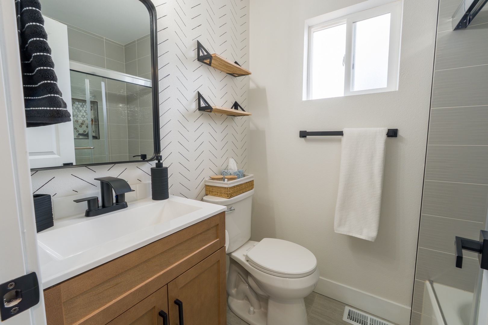 Step into your spa-like bathroom with modern herringbone tile, warm wood vanity, and sleek black fixtures for ultimate relaxation.