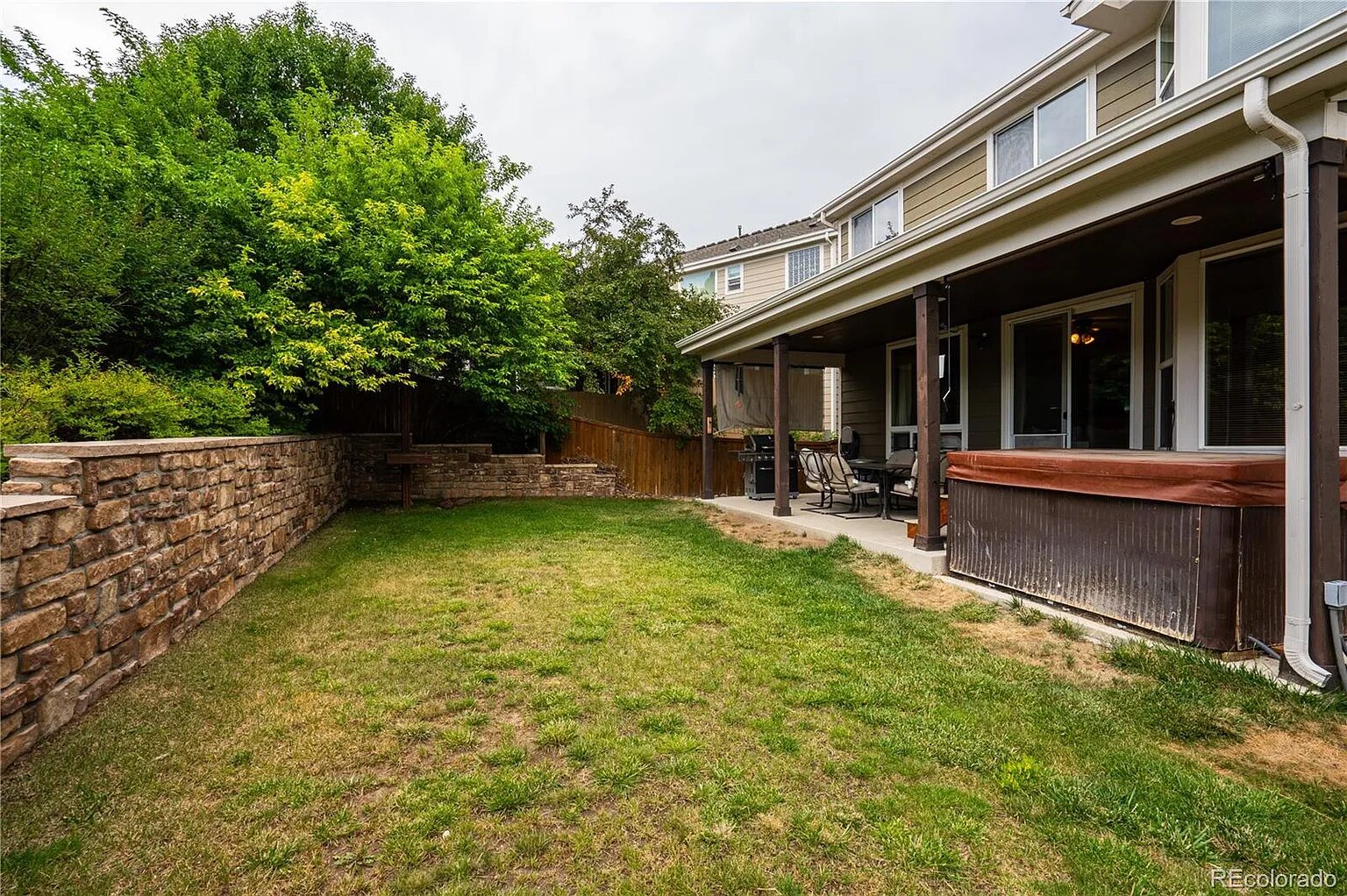 Your private backyard oasis features a spacious lawn perfect for outdoor activities, surrounded by mature trees and enclosed by elegant stonework.