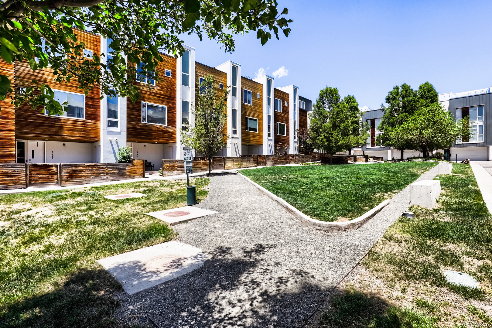 Modern townhomes with warm wood exteriors surround a peaceful courtyard with walking paths and mature trees—a welcoming residential neighborhood perfect for a comfortable stay.