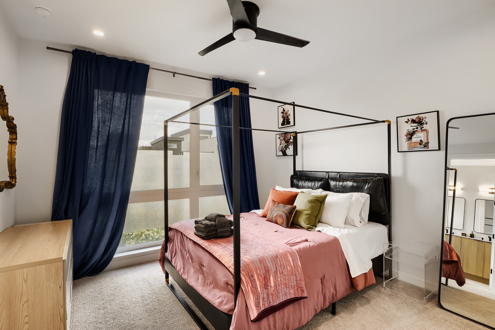 Drift off in this stylish canopy bed, wrapped in soft blush and coral tones. Your private retreat feels airy and modern, with natural light streaming through the windows and a ceiling fan keeping you comfortable.