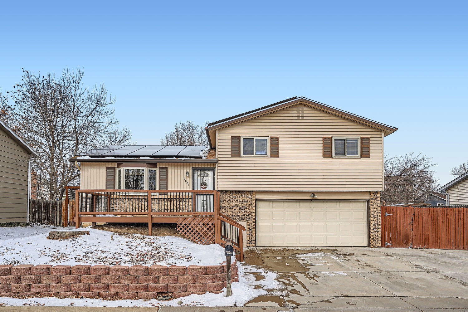 A welcoming split-level home with a spacious wooden deck and attached two-car garage, nestled in a quiet residential neighborhood with seasonal winter surroundings.