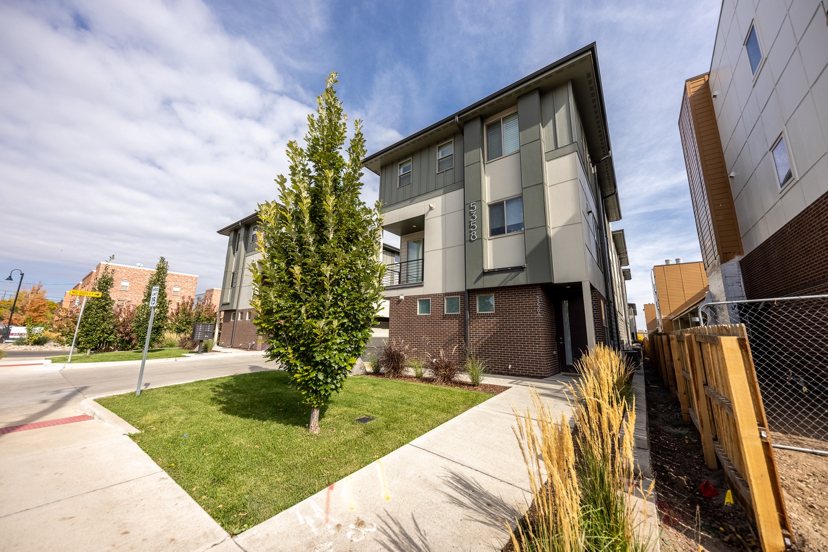 Modern three-story building with contemporary architectural design, featuring mixed materials including brick, metal panels, and glass. The property is located in a residential neighborhood with landscaped front lawn and young trees.