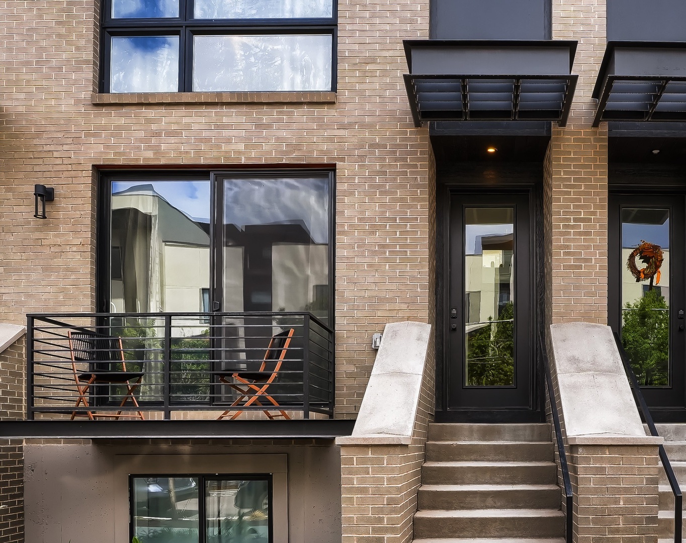 Modern brick townhome entrance features stylish black-framed doors and a welcoming private balcony where you can enjoy morning coffee or evening chats.