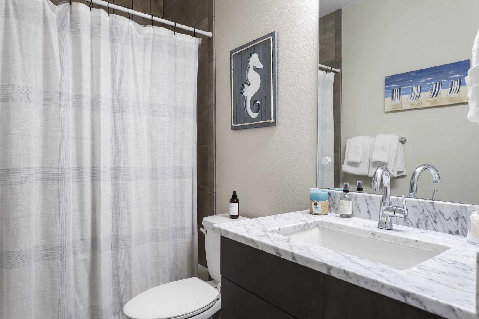 Fresh towels await as you unwind in your stylish bathroom featuring elegant marble countertops and coastal artwork.