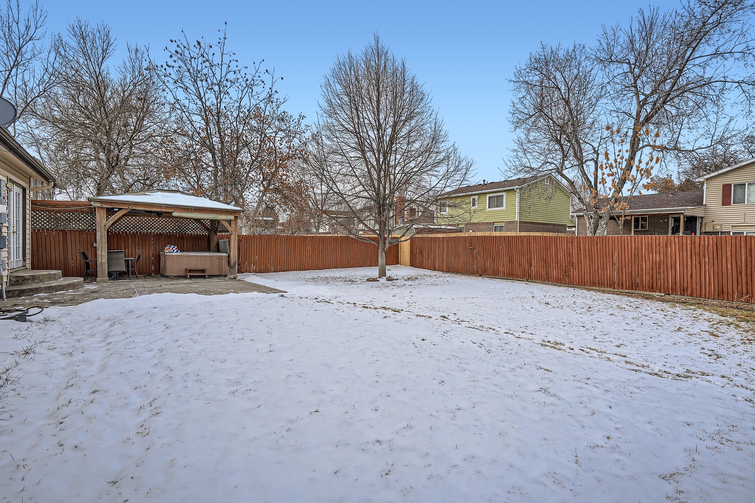The property features a spacious backyard with mature trees, wooden fencing for privacy, and a covered patio structure during the winter season.