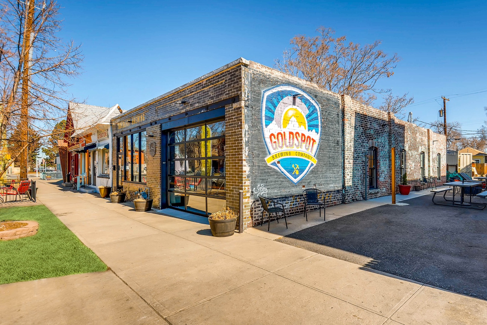 The Goldspot Brewing Company building stands prominently in the neighborhood, its brick exterior adorned with a vibrant mural and outdoor seating ready for visitors.