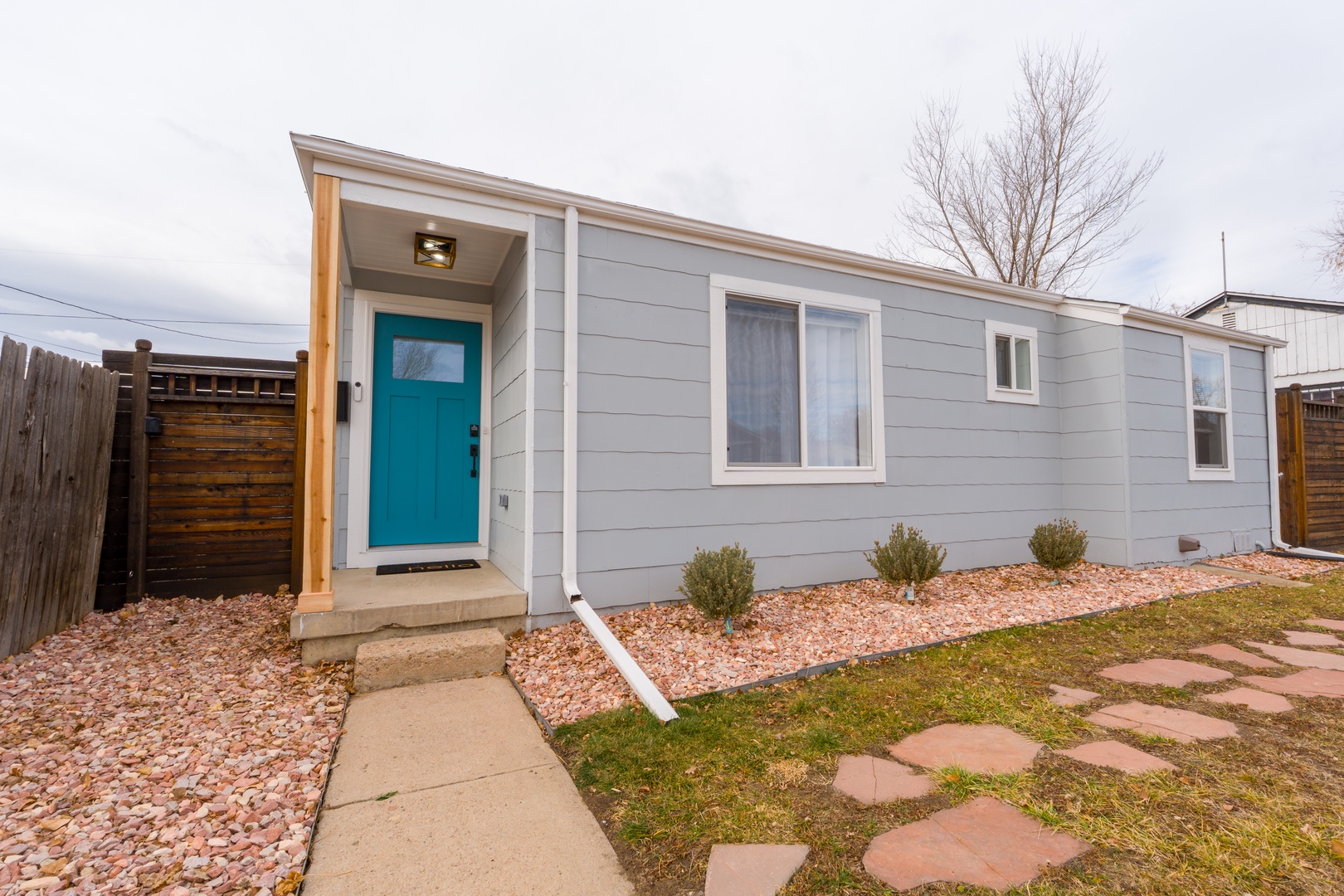 Modern gray exterior with welcoming turquoise door and desert landscaping in a quiet residential neighborhood.