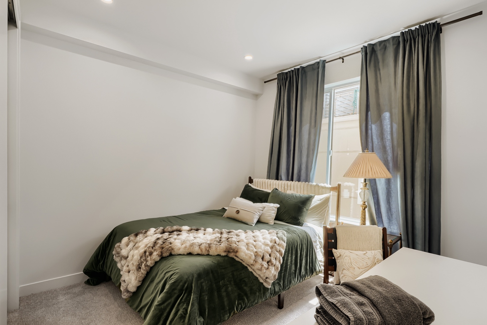 Sink into the plush textures of your serene bedroom, where emerald-toned linens and soft lighting create a peaceful retreat. Natural light filters through elegant curtains, making this your perfect sanctuary to unwind.