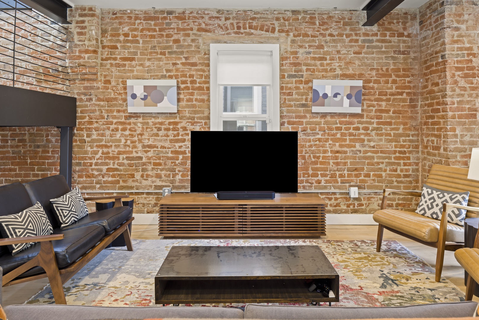 Relax in your stylish living area featuring exposed brick walls, modern furniture, and entertainment center for cozy evenings.