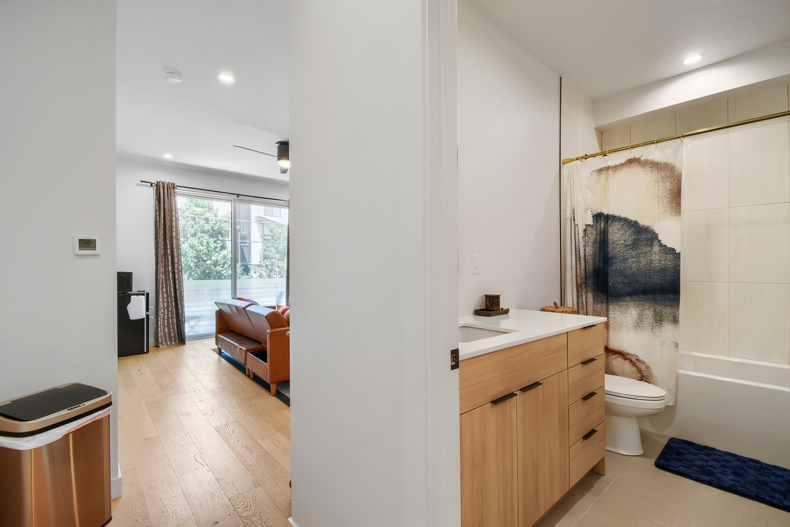 Your modern retreat features a sleek bathroom with contemporary finishes, flowing seamlessly into an open living area where warm light filters through large windows, inviting you to relax and unwind.