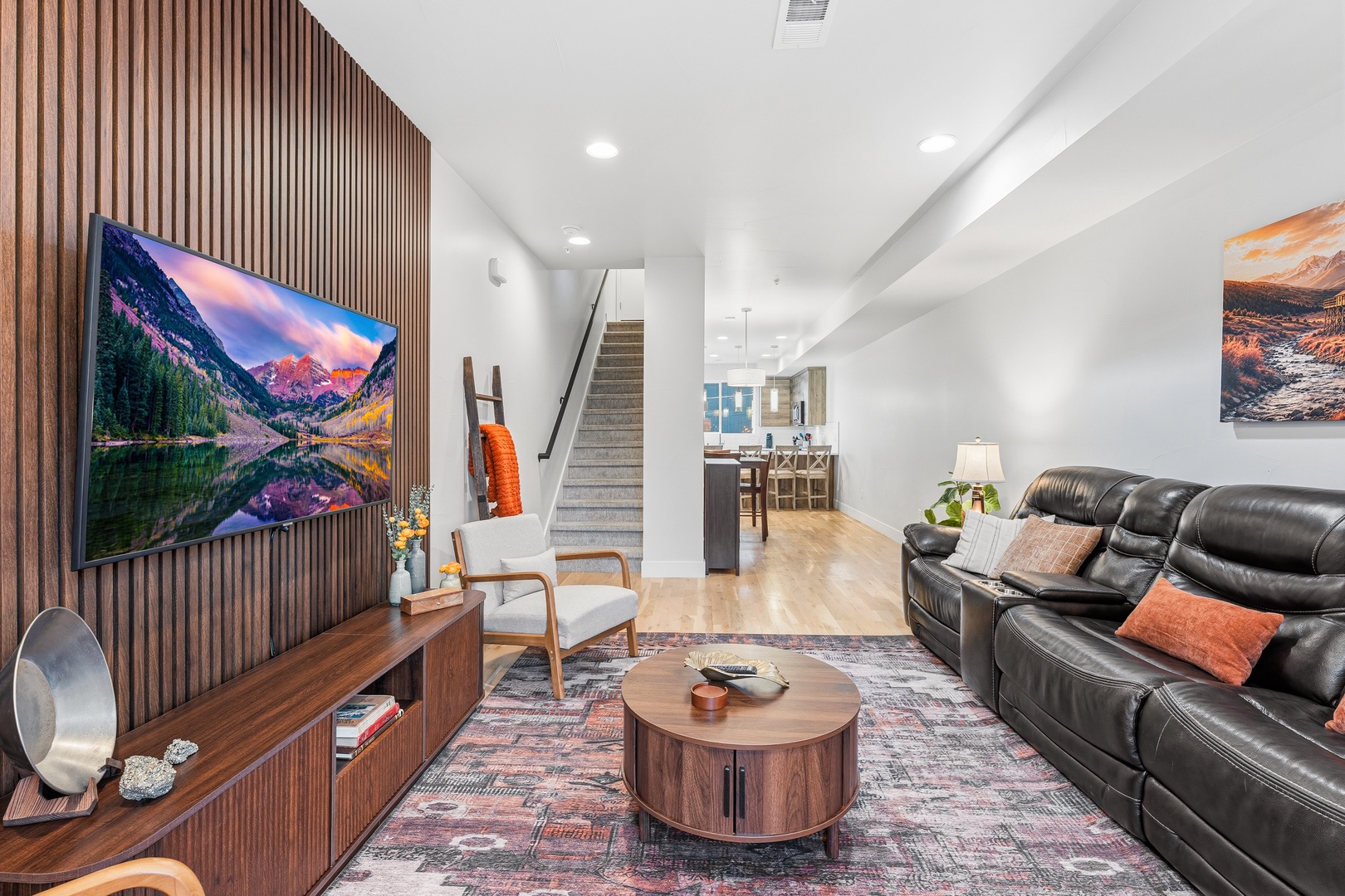 Unwind in your spacious living room featuring plush leather seating, a stunning wood-paneled entertainment wall, and natural light flowing through the open layout—perfect for cozy evenings and leisurely mornings.