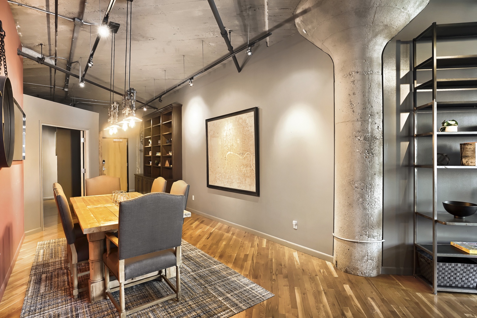 Your dining area features exposed concrete pillars, industrial track lighting, and warm wood accents that create an inviting urban loft atmosphere for meals and conversation.