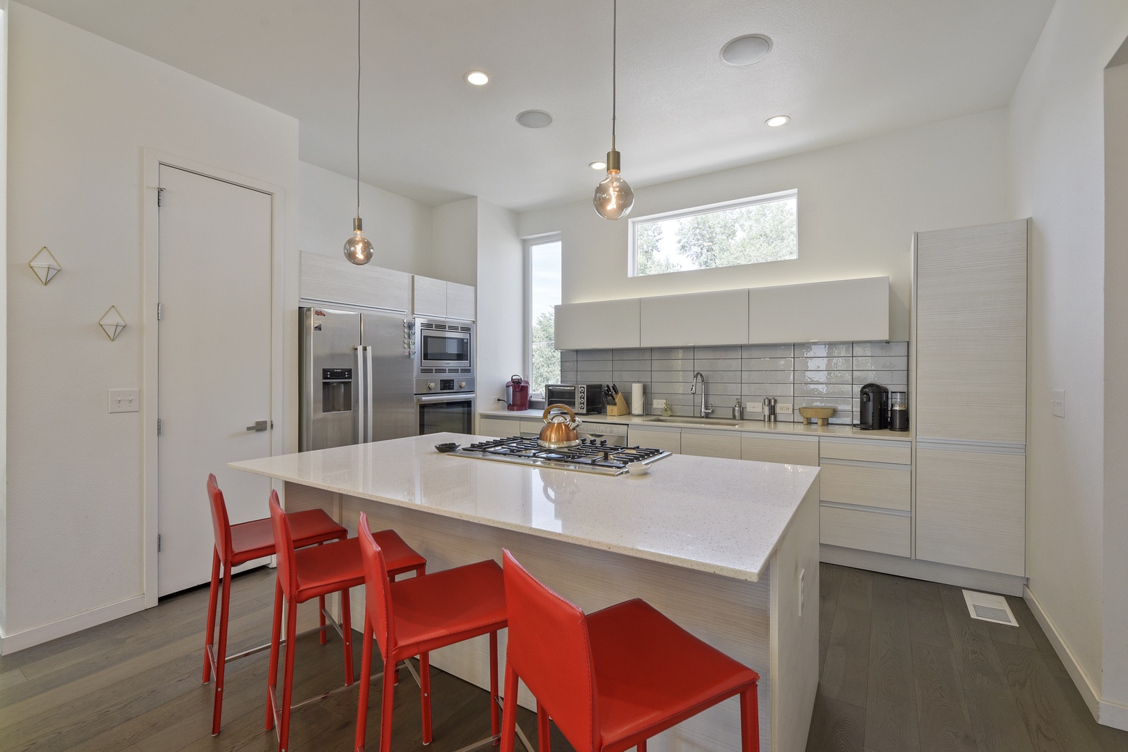 Gather around this modern kitchen island with sleek white countertops and a professional gas range. Natural light fills the space, making your morning coffee or evening meal prep a bright, inviting experience.
