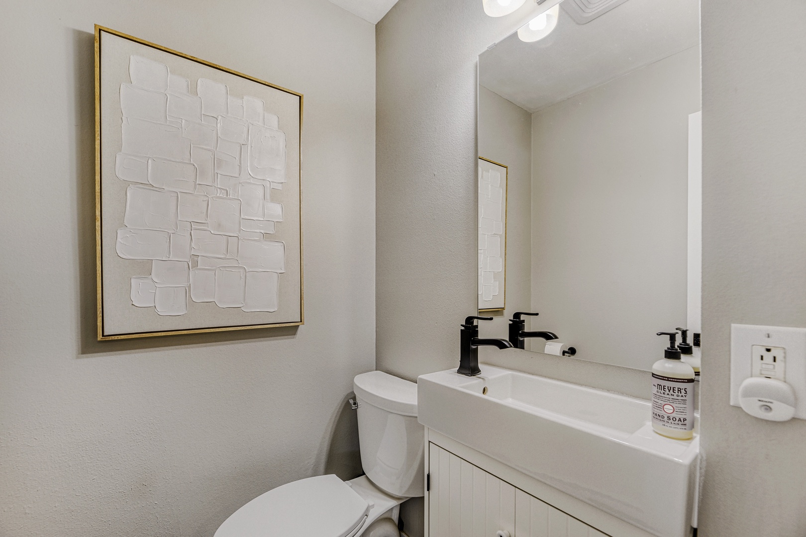 You'll appreciate the clean, modern design of this bathroom, complete with elegant fixtures, a vanity with Mrs. Meyer's hand soap, and contemporary artwork adding a stylish touch.