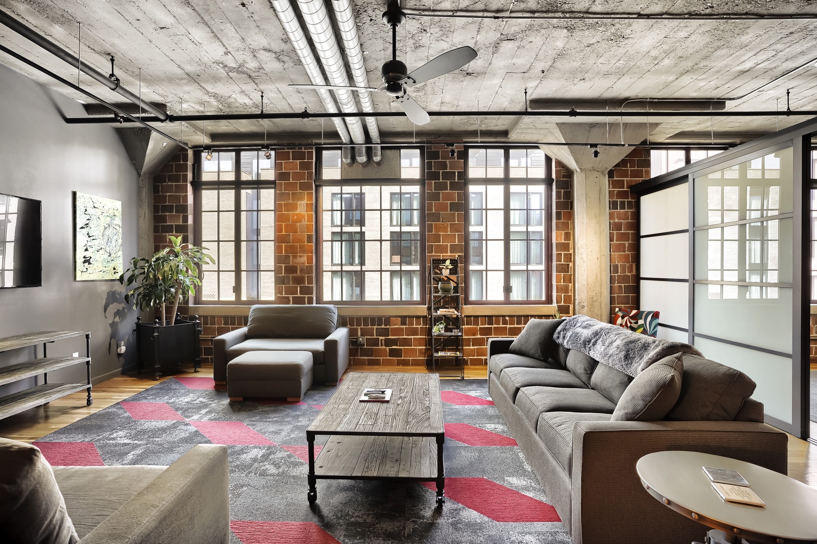 Sink into plush sofas in your spacious urban loft, where exposed brick, soaring ceilings, and natural light create an inviting industrial-chic haven perfect for relaxing.