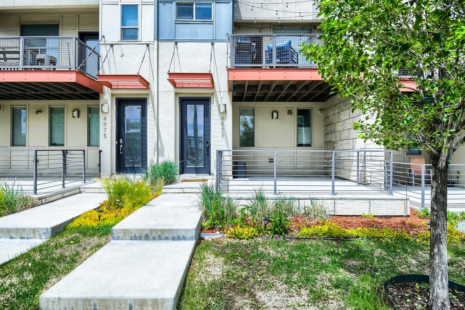 Modern multi-unit property featuring private entrances, outdoor balconies, and landscaped grounds with native plants and mature trees throughout the community.