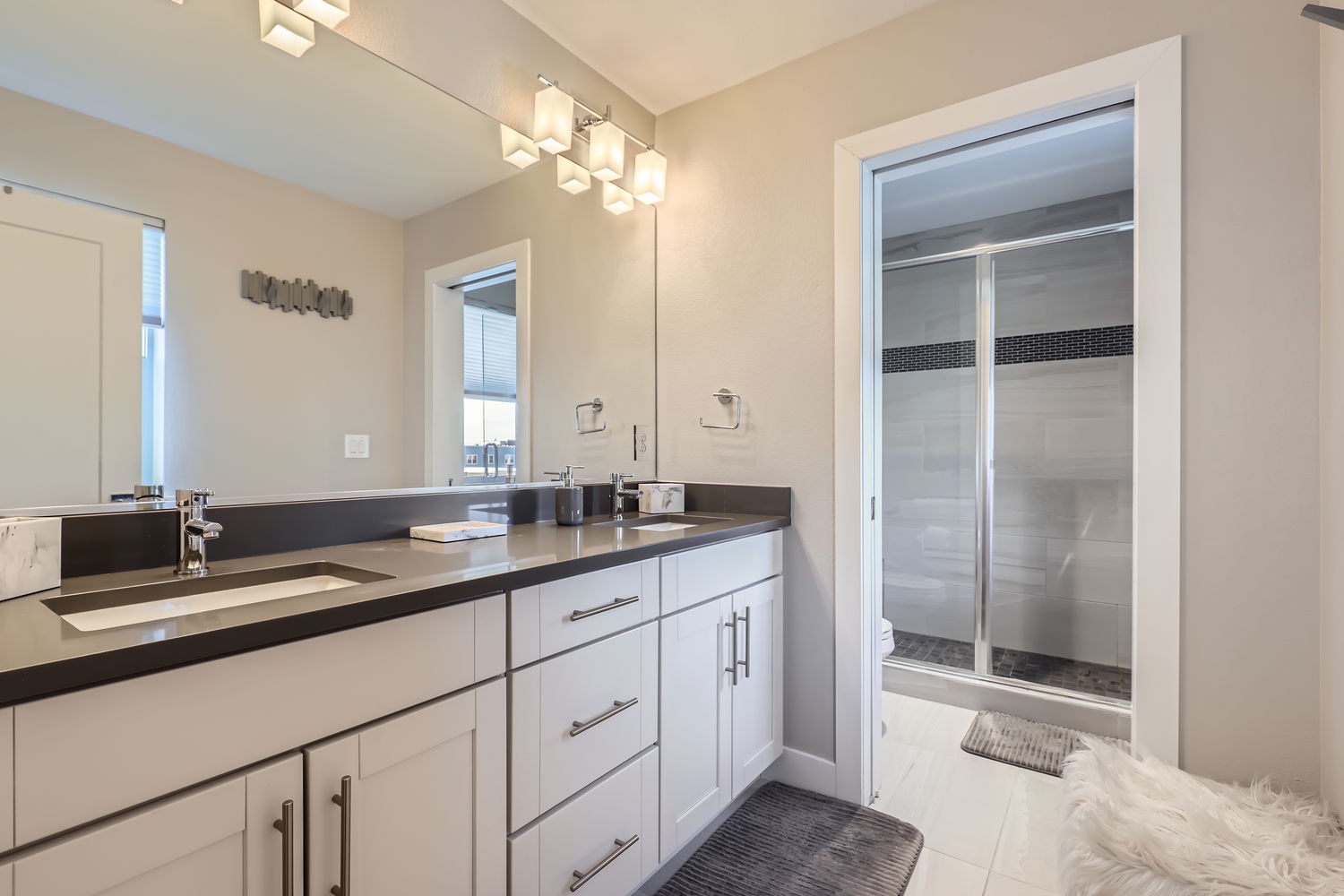 Your elegant dual-sink vanity gleams under modern lighting, while the spacious walk-in shower with sleek tile accents awaits to refresh you after a long day exploring.
