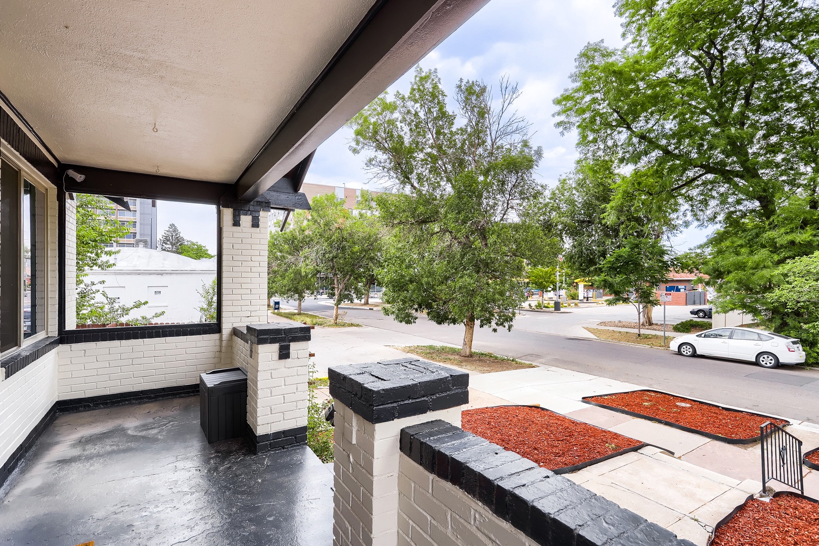 A covered porch area providing a shaded outdoor retreat with views of the tree-lined residential street.
