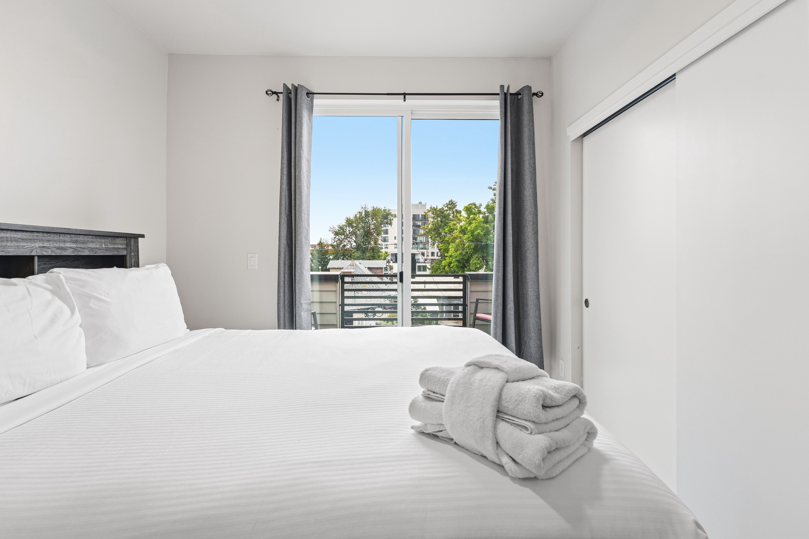 Sink into crisp linens and enjoy the leafy view from your private balcony through the floor-to-ceiling windows. This bright, serene bedroom invites you to unwind in comfort and style.