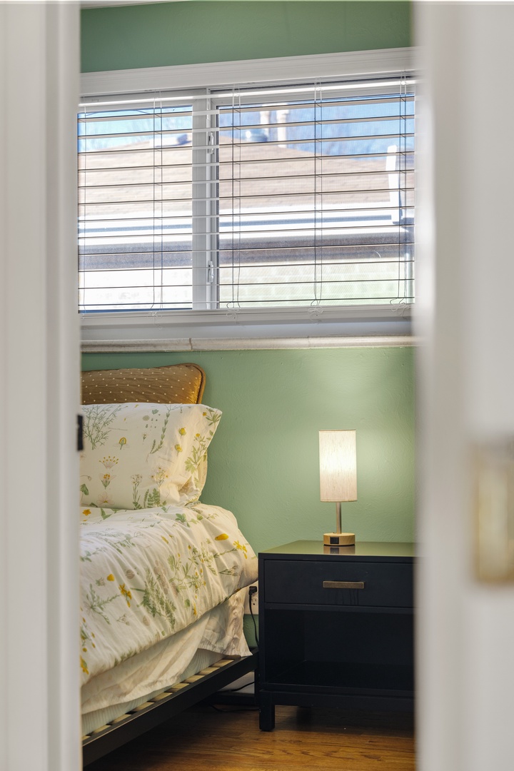 Your cozy bedroom retreat features cheerful botanical bedding and soft natural light filtering through stylish blinds.