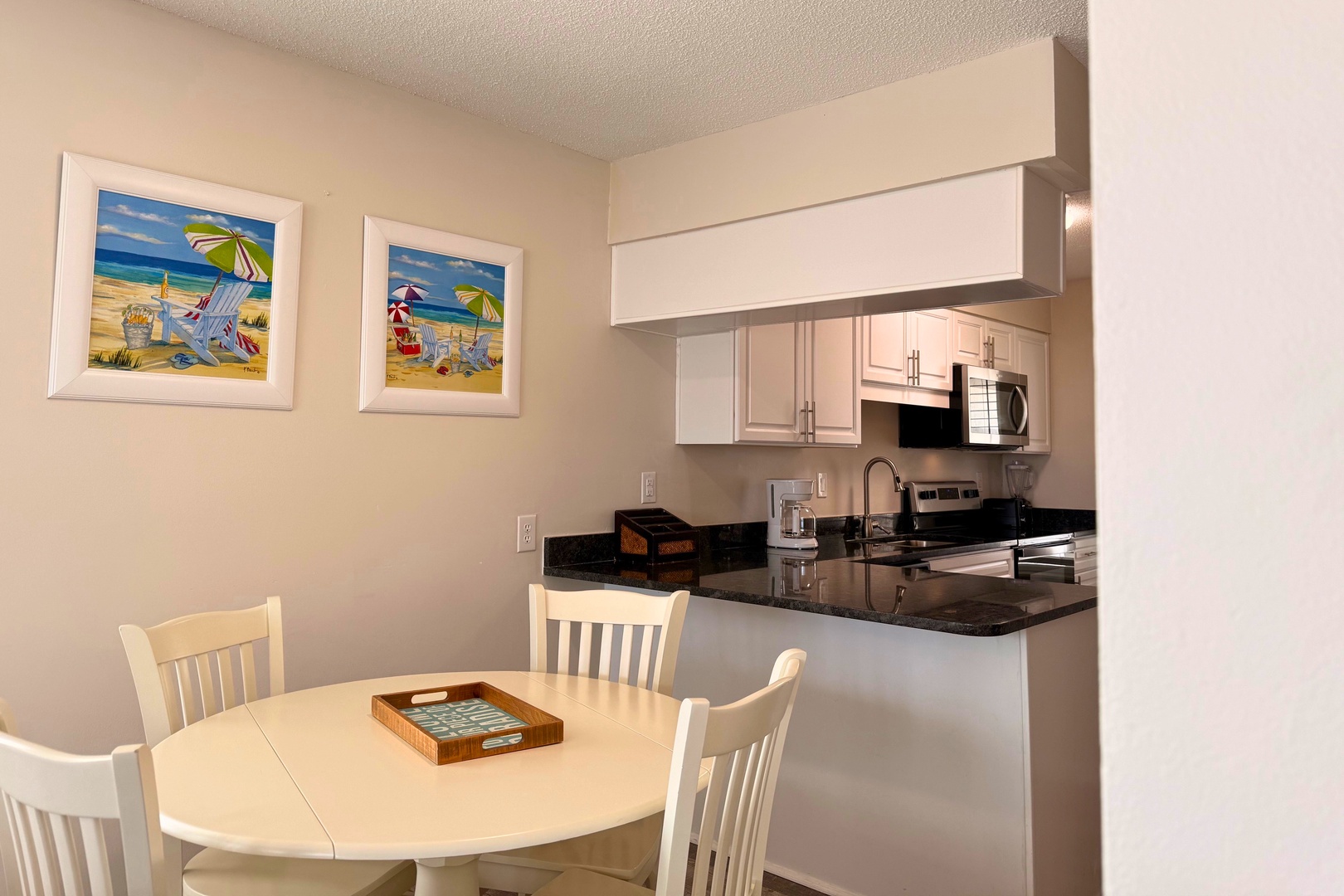 Your bright, fully equipped kitchen opens to a cozy dining nook where beachy artwork sets a relaxed, coastal mood for meals together.