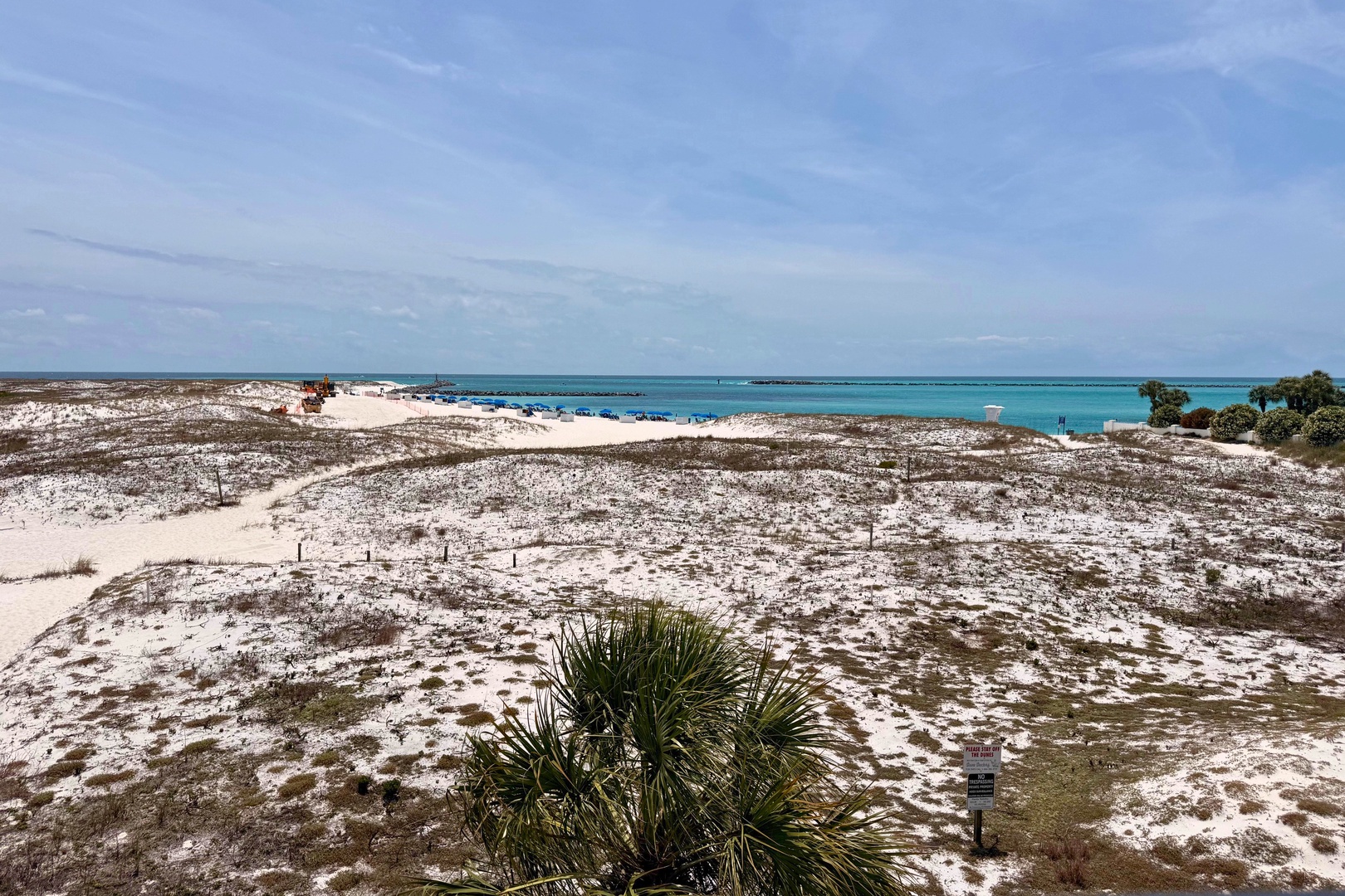 A coastal property location features sandy terrain, native vegetation, and stunning turquoise waters visible from the surrounding area.