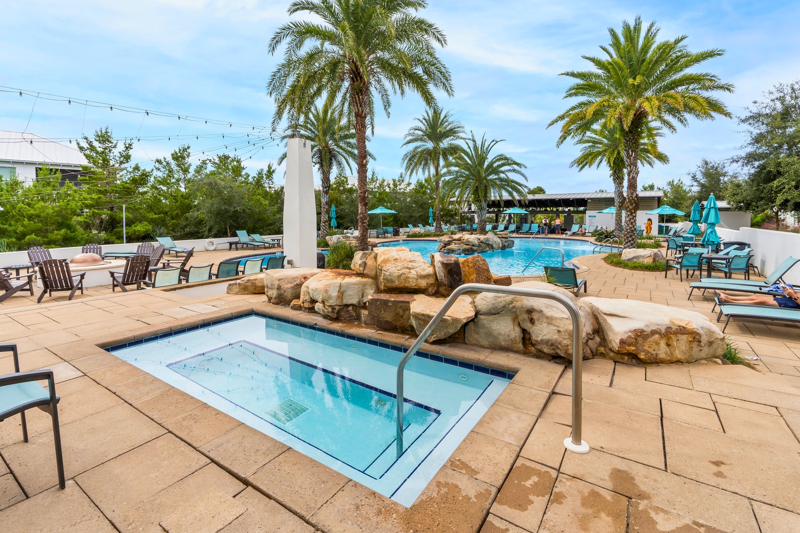 Soak up tropical vibes at this stunning pool complex featuring a relaxing hot tub, main swimming pool with rock features, and palm-lined lounging areas.