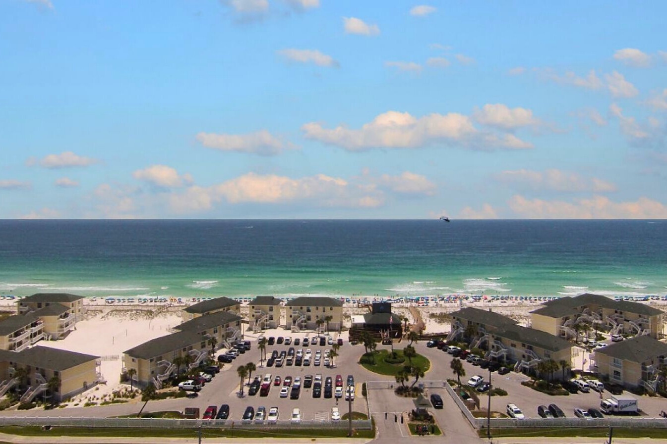 Aerial view of beachfront property complex with direct beach access and expansive parking facilities.