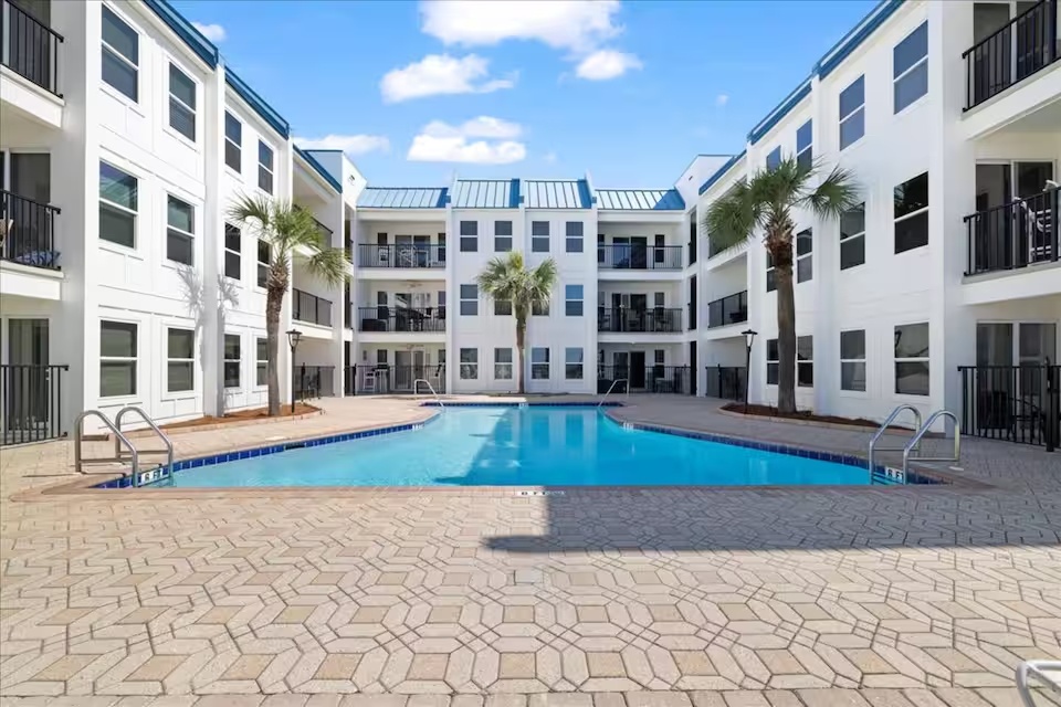 Beautiful resort-style courtyard pool surrounded by palms and lounge seating—your private oasis near the beach.