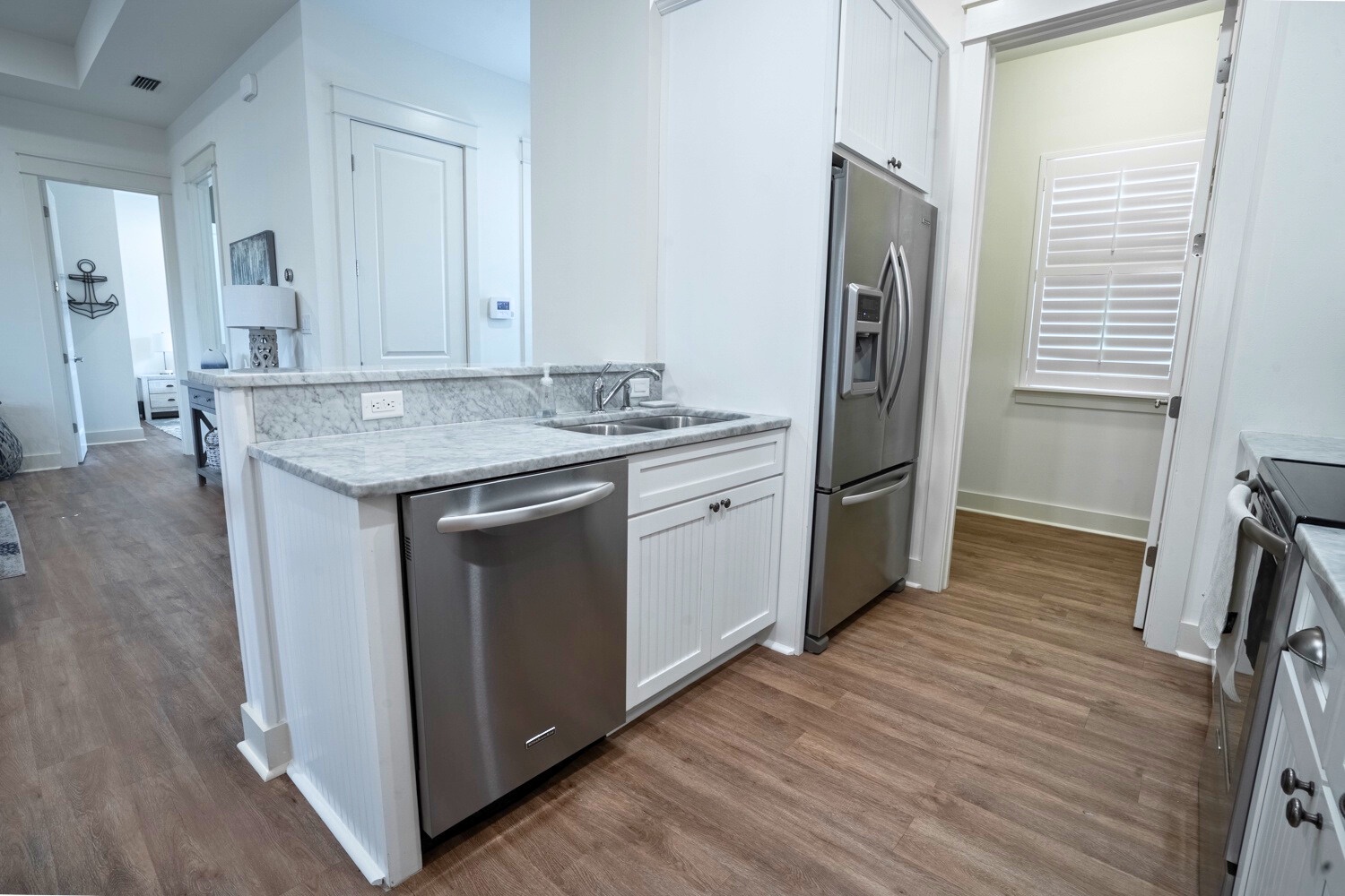 Bright coastal kitchen with white cabinets, granite counters, stainless appliances, and warm wood floors throughout.