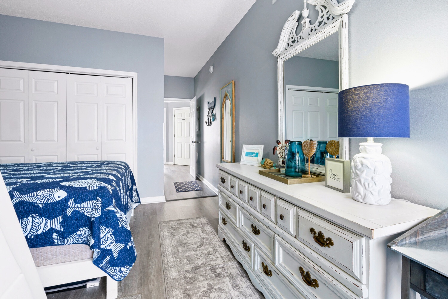 Your serene bedroom features soothing blue walls, elegant white furniture, and thoughtful coastal touches that create the perfect retreat for relaxation.