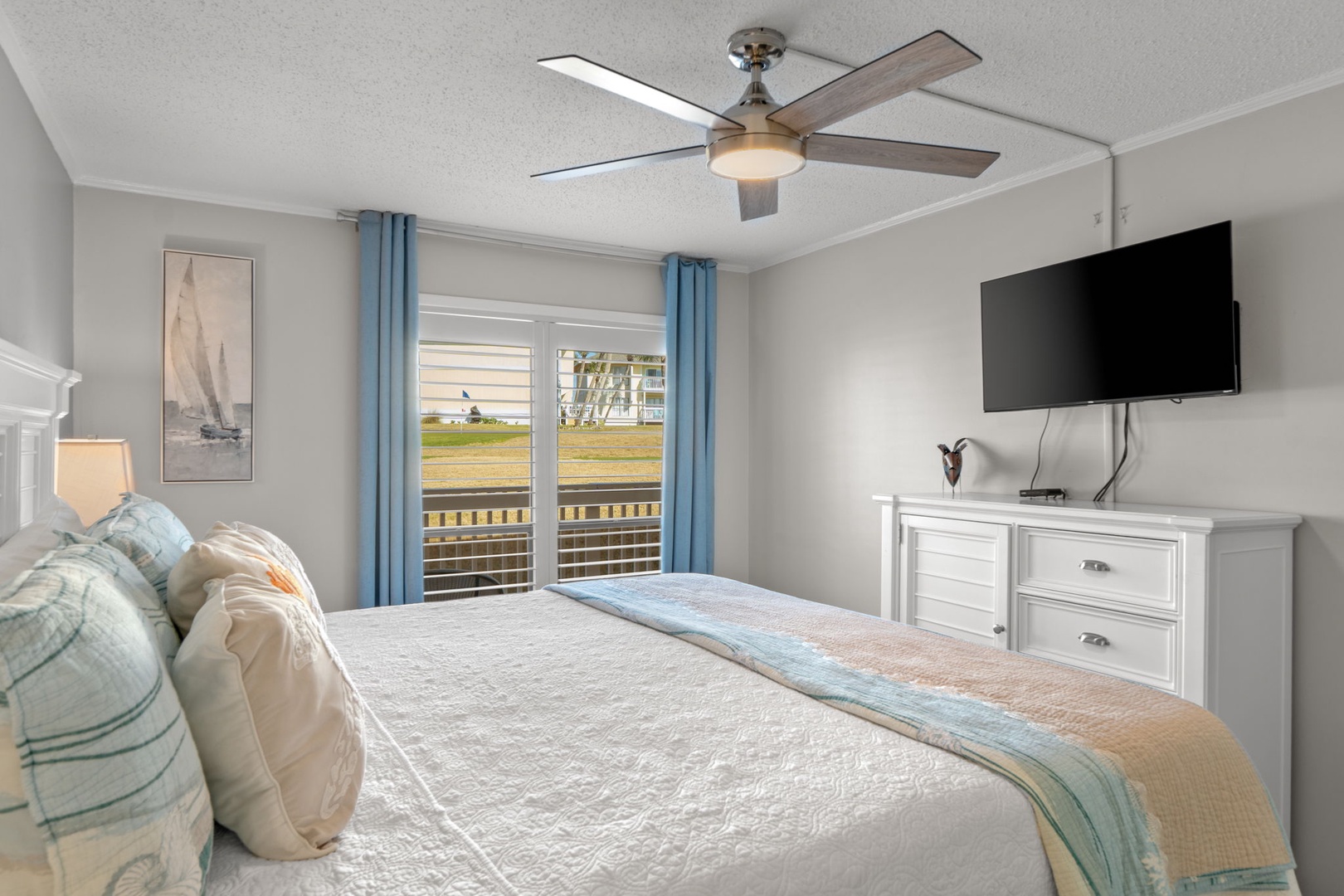 Wake up to peaceful golf course views from the comfort of the primary bedroom featuring a king bed, coastal décor, and direct access to the private patio for a relaxing indoor-outdoor retreat.