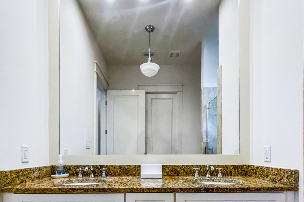 Clean coastal bathroom with double vanity, granite countertops, bright lighting, and crisp white finishes.