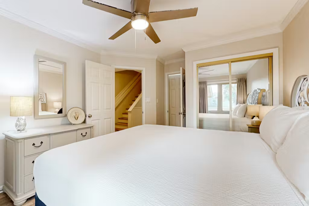 Bright, inviting bedroom with crisp linens, a ceiling fan, mirrored closet doors, and convenient access to the adjoining living areas.