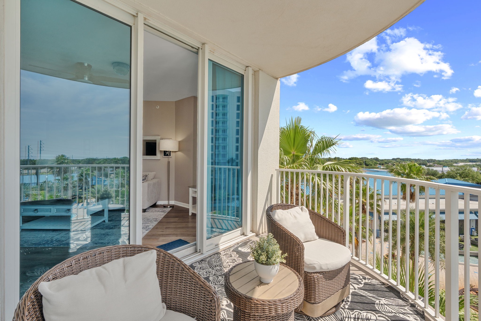 Unwind in your private balcony retreat with cozy wicker seating, tropical palms, and sweeping water views—your perfect spot to soak up the sunshine and serene scenery.