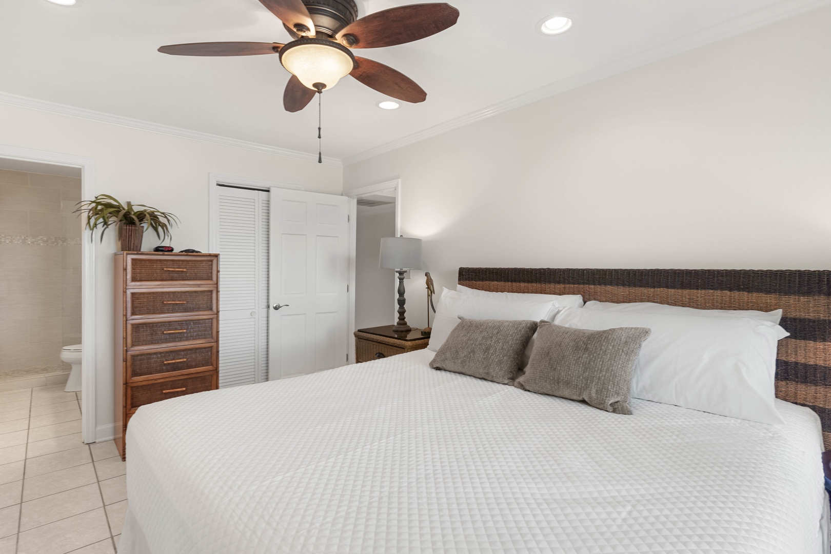Drift off in your peaceful bedroom with crisp white linens, natural wicker headboard, and cooling ceiling fan for perfect comfort.