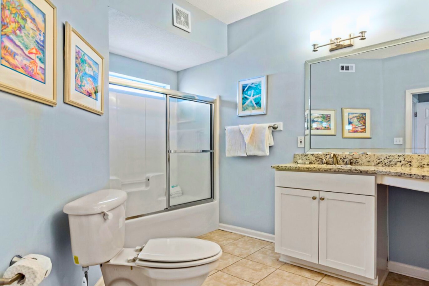 Unwind in your spacious bathroom featuring granite counters, glass shower doors, and cheerful artwork creating a spa-like retreat.